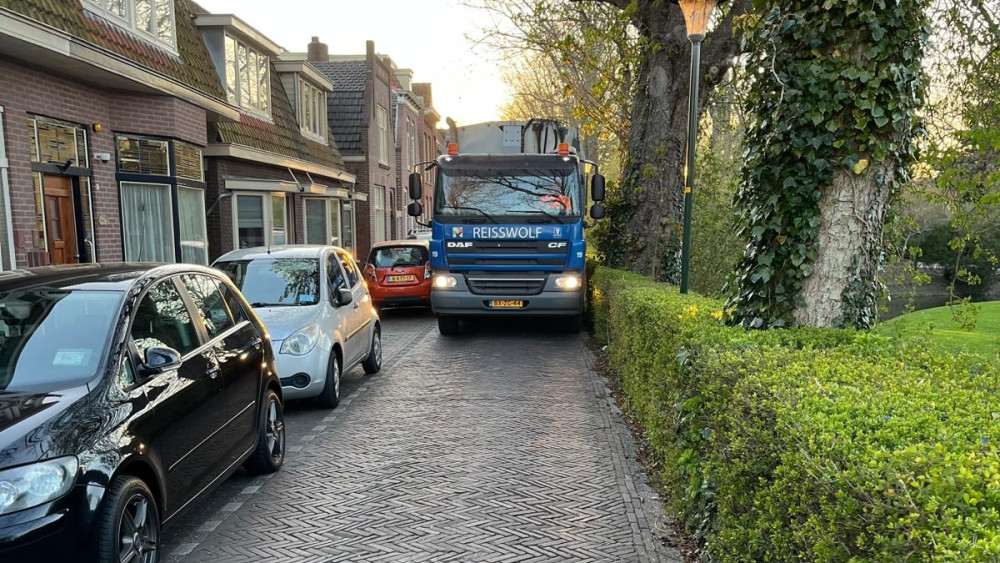 De oud papierwagen kan maar net langs de geparkeerde auto's